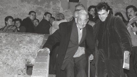 El filòleg i lingüista Joan Coromines a l'ermita de Sant Pau de Sant Pol de Mar, en l'acte d'homenatge al seu pare, Pere Coromines. L'artista Perejaume l'ajuda a baixar les escales. Sant Pol de Mar. 25 de gener de 1992 