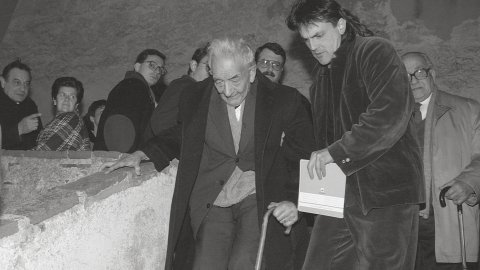 El filòleg i lingüista Joan Coromines a l'ermita de Sant Pau de Sant Pol de Mar, en l'acte d'homenatge al seu pare, Pere Coromines. L'artista Perejaume l'ajuda a baixar les escales. Sant Pol de Mar. 25 de gener de 1992 
