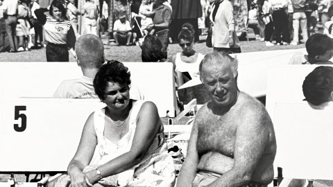 Turistes alemanys asseguts en uns patinets de la platja de Calella mentre al passeig Manuel Puigvert hi ha una trobada de gegants per la festa major. 1989-1990. Foto: Saül Gordillo (El Nunci)